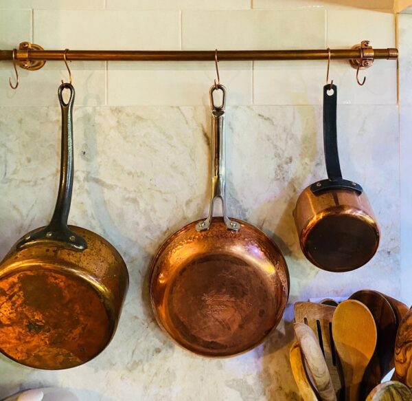 Copper pot rack with pots and pans hanging on a marble kitchen wall
