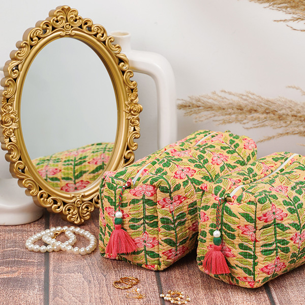 Photograph of a toiletry makeup bag set featuring a pink and green floral pattern against a buttery yellow ground, embellished with a pink and green tassel on the zipper pull