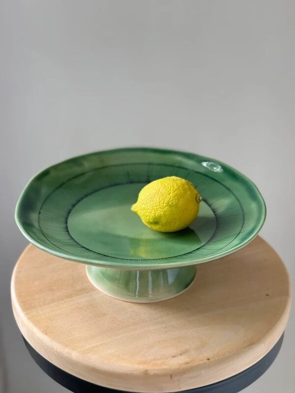 Photograph of a green ceramic fruit bowl with a lemon to demonstrate the use of a dish pedestal for round table decor ideas