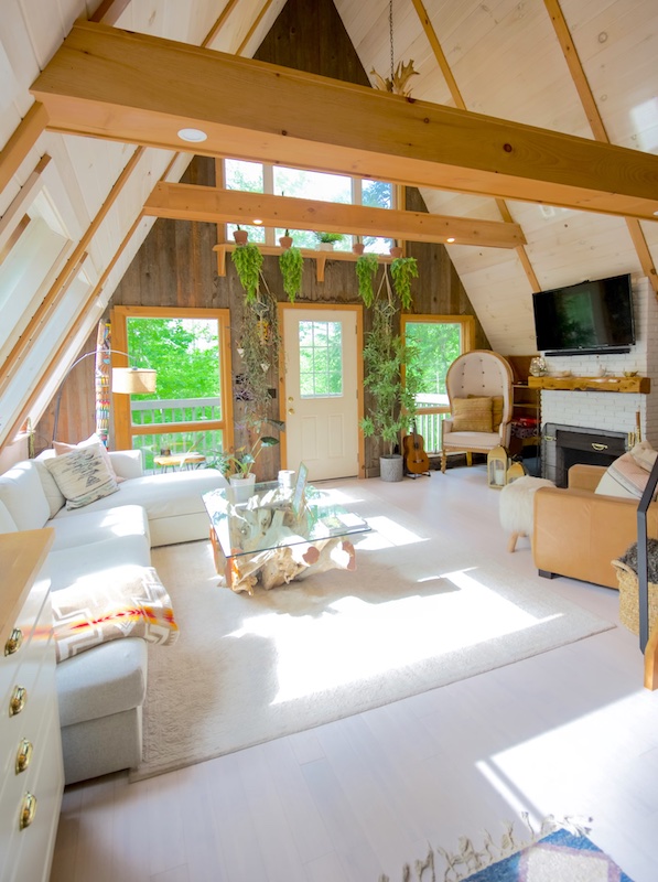 Photograph of a wooden lake house cabin with high ceilings featuring indoor plants and an earthy color palette