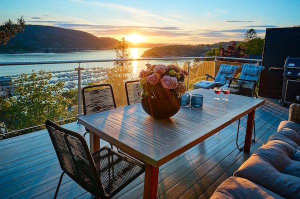 Photograph of a lake house outdoor space featuring dining tables, chair, lounges, and a cushioned sofa