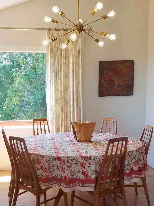 Photograph of a dining room with a round table covered in a tropical tablecloth and topped with a natural wooden bowl to demonstrate the use of wooden bowls as round table decor ideas