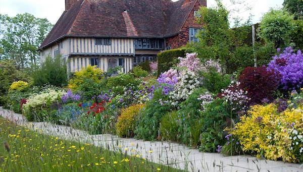 Photograph of an English botanical garden featuring bushes of various plants that line the row leading up to the English cottage home