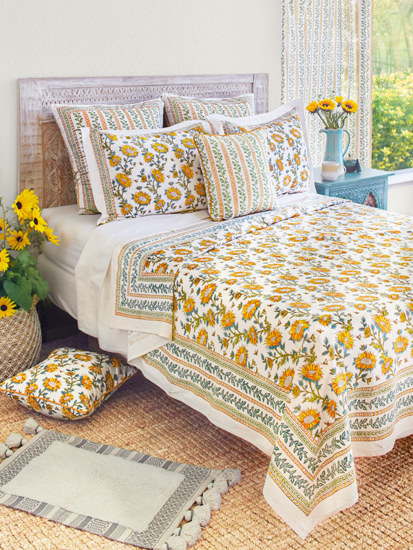 Photograph of a bed featuring sunflower bedding showcassing a botanic sunflower and bee print in yellow, orange, green, teal, and white with a striped vine border