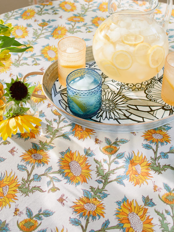 Photograph of a sunflower print tablecloth with a lemonade pitcher and summery elements that complement the botanic print