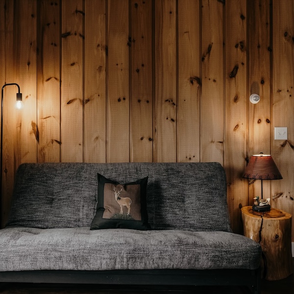 Sofa with deer pillow, wood panel wall, and wood side table